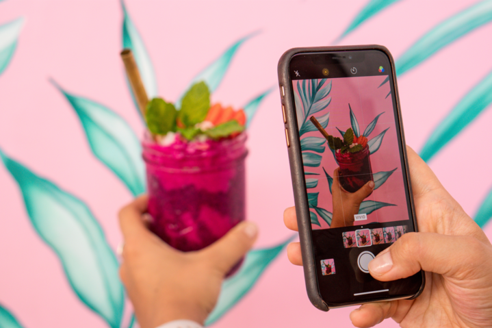 Woman learning how to master Instagram ads and taking photo of the colorful smoothie on her mobile phone